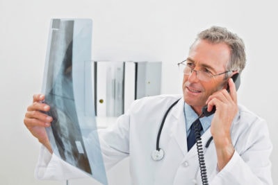 Male doctor looking at x-ray picture while using the telephone at medical office