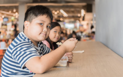 Obese brother and sister eating box lunch in food court, fastfood concept
