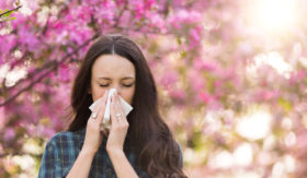 Frau putzt sich die Nase mit einem Taschentuch, weil sie eine Allergie hat.