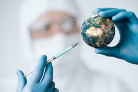 Arzt zielt mit Spritze auf Miniatur der Erde