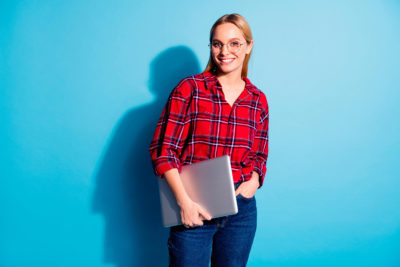 Portrait of nice charming cute attractive winsome cheerful cheery teen girl wearing checked shirt carrying laptop isolated on teal turquoise bright vivid shine background.
