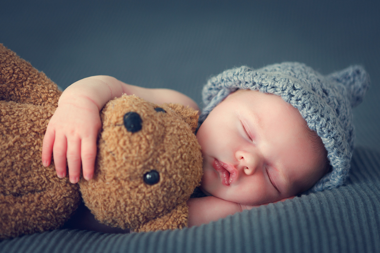 sleeping newborn baby on a blanket with a teddy