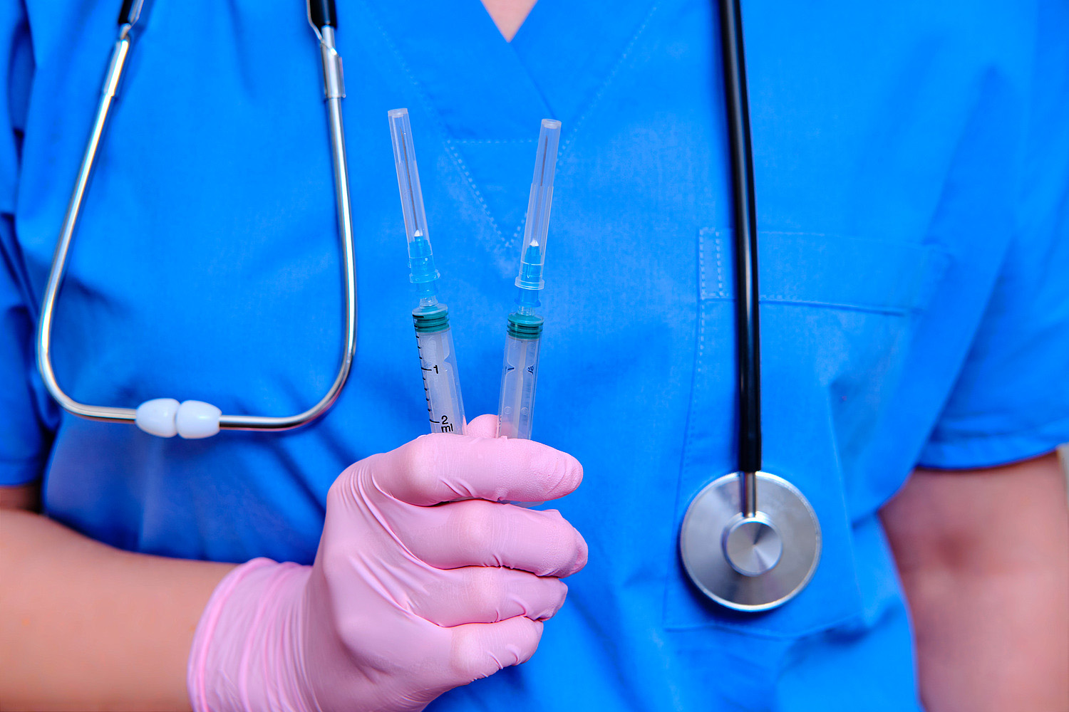 A doctor in a blue uniform with syringes in his hand, close-up. Medic with coronavirus vaccine, concept of medication for flu virus