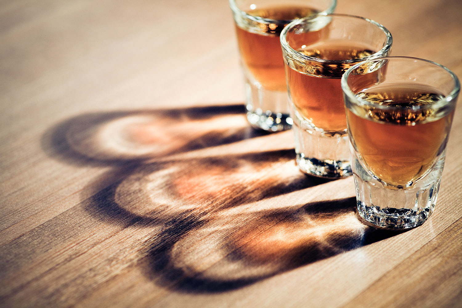 three shot glasses full of dark colored alcohol on top of a bar table. The shot could be whiskey, dark rum, tequila, cognac, or bourbon.