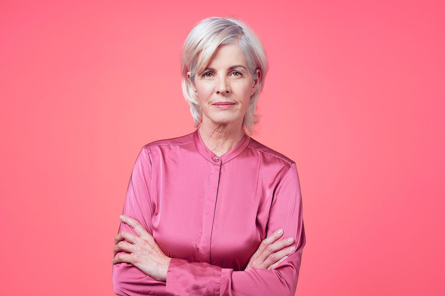 Portrait of a confident elderly woman standing against a pink background inside of a studio