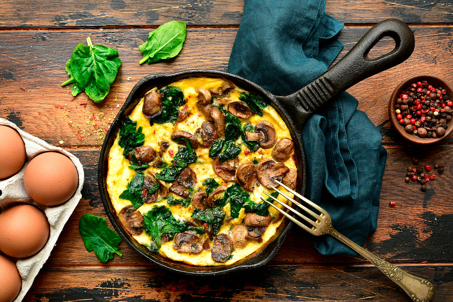 Omelette with mushrooms and spinach in a cast iron pan on a dark rustic wooden background.Top view with copy space.