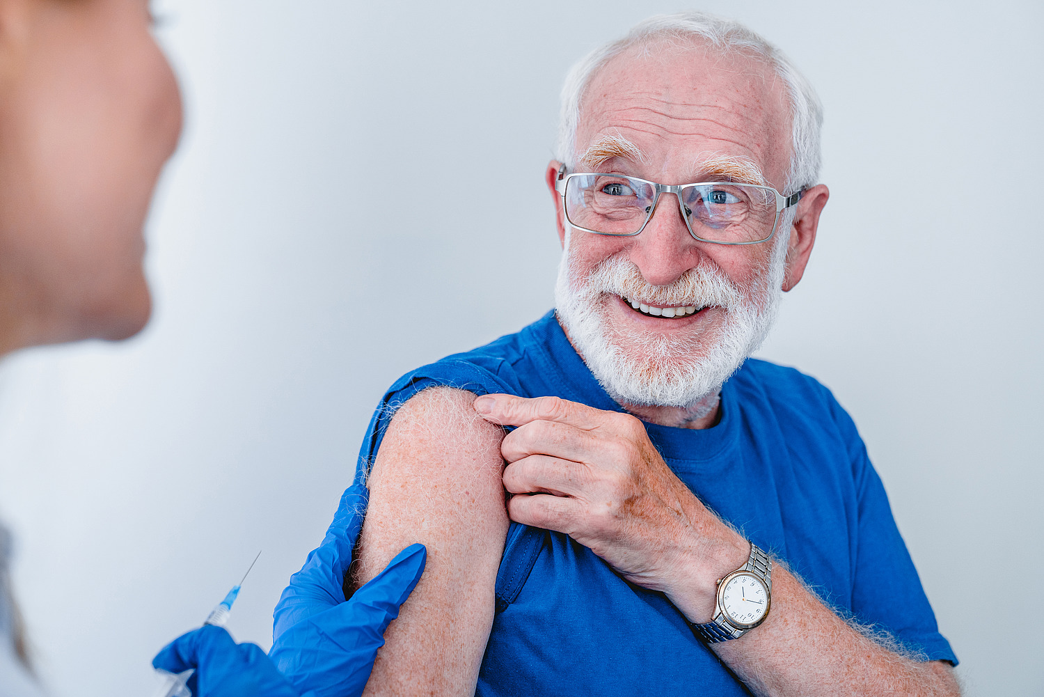 Smiling elderly patient in glasses is getting ready for injection isolated over white background